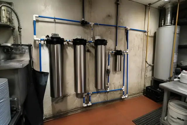 Whole-home PFAS filtration system with stainless steel filters and blue piping in a Tempe, AZ restaurant utility area.