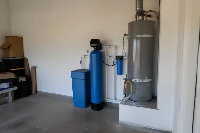 Whole-home water filtration system with blue tank and PVC piping installed in a residential garage in Gilbert, AZ.