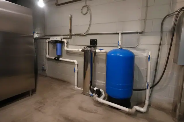 Whole-home water filtration system with blue tank and PVC piping in a Scottsdale, AZ utility room.