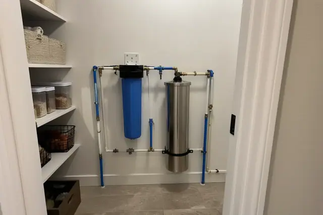 Whole-home water filtration system with blue housing and stainless steel tank installed in a Phoenix, AZ pantry.