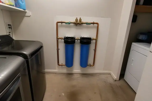 Whole house water filtration system with blue housings and copper pipes installed in a laundry room in Tempe, AZ.
