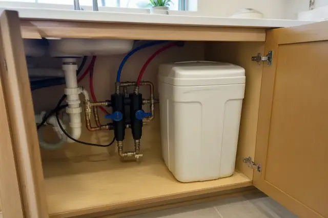 Water softener installation with copper and PEX plumbing inside a kitchen cabinet in Tempe, AZ.
