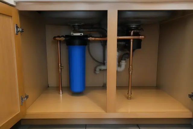 Whole-house water filtration system with blue filter and copper pipes installed under a kitchen sink in Tempe, AZ.
