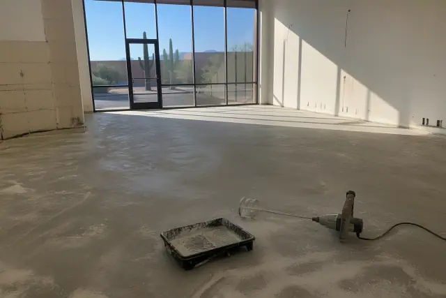 Sanded concrete floor prepared for metallic epoxy installation in a Tucson, AZ retail showroom with jobsite tools.