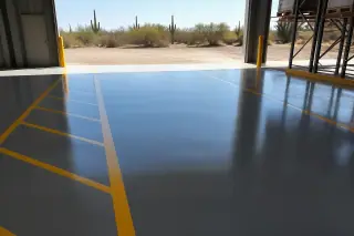 Glossy industrial epoxy floor with lane markings and Saguaro desert views through an open warehouse door in Tucson, AZ.