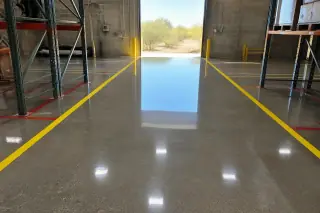 High-gloss epoxy warehouse floor with marked lanes and desert views through an open bay door in Tucson, AZ.