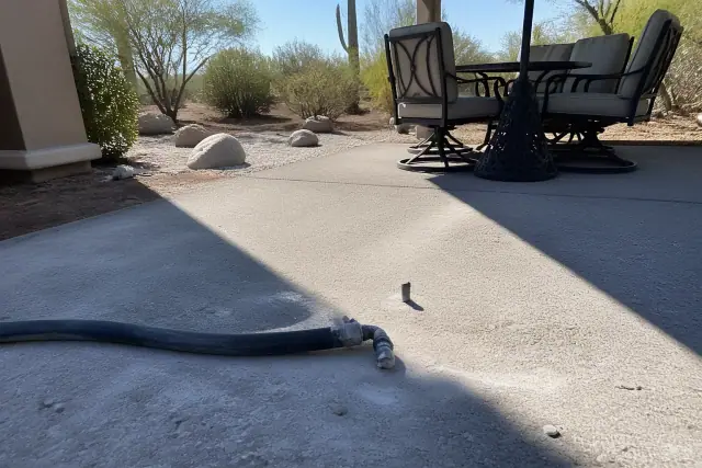 Concrete leveling and repair work on a backyard patio in Tucson, AZ, featuring an injection port and mud-jacking hose.
