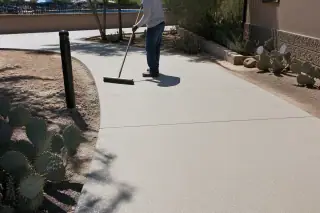 Worker using a push broom on a finished anti-slip resurfaced walkway in Tucson, AZ with prickly pear cacti.