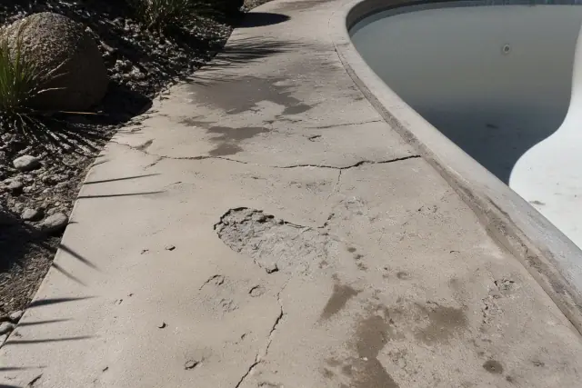 Concrete walkway with cracks, spalling, and oil stains surrounding a drained swimming pool in Tucson, AZ.