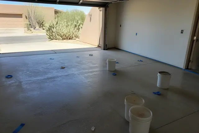 Empty two-car garage prepped for epoxy floor coating with mixing buckets and cacti visible in Tucson, AZ.