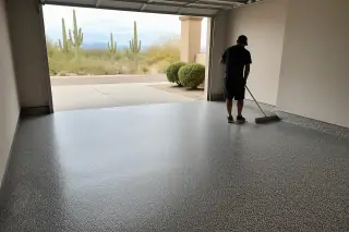 Technician using a push broom on a finished flake epoxy garage floor in a Tucson, AZ home with Saguaro cacti outside.
