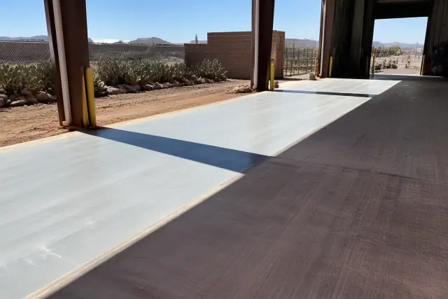 Industrial epoxy flooring prep on a warehouse loading dock with grinding marks and prickly pear cacti in Tucson, AZ.