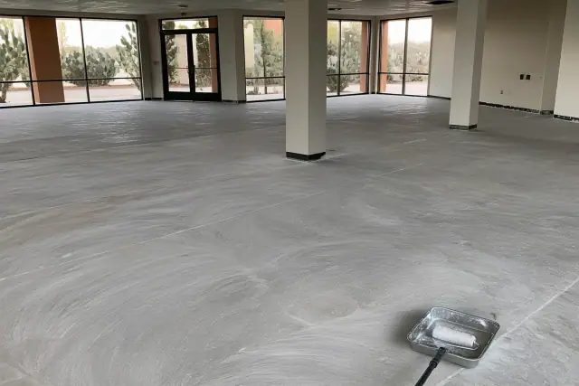 Sanded concrete floor prepared for polyaspartic coating at a Tucson, AZ retail showroom with cactus visible outside.