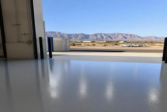 Glossy industrial epoxy flooring at a warehouse loading dock in Tucson, AZ with desert sagebrush and mountains behind.