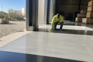 Contractor inspecting a cured epoxy floor in a Tucson, AZ warehouse with prickly pear cacti outside.