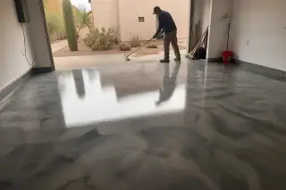 Technician using a dust mop on a glossy metallic epoxy garage floor with Sonoran desert plants visible in Tucson, AZ.