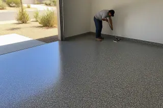 Contractor wiping down a finished flake epoxy garage floor in a Tucson, AZ home with desert plants visible outside.