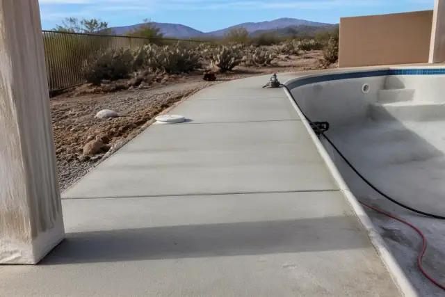 Drained swimming pool deck with concrete surfaces ready for sealant, featuring desert landscaping in Marana, AZ.