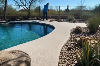 Technician cleaning a textured pool deck coating in a sunny residential backyard in Tucson, AZ.