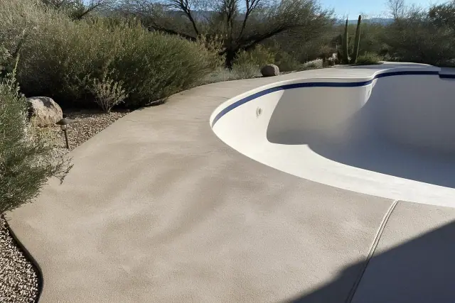 Drained swimming pool deck undergoing resurfacing and repair in Tucson, AZ, with desert plants in the background.