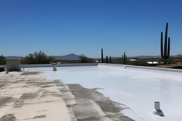 Freshly applied white acrylic roof coating on a flat rooftop under the bright sun in Tucson, AZ, with distant cacti.