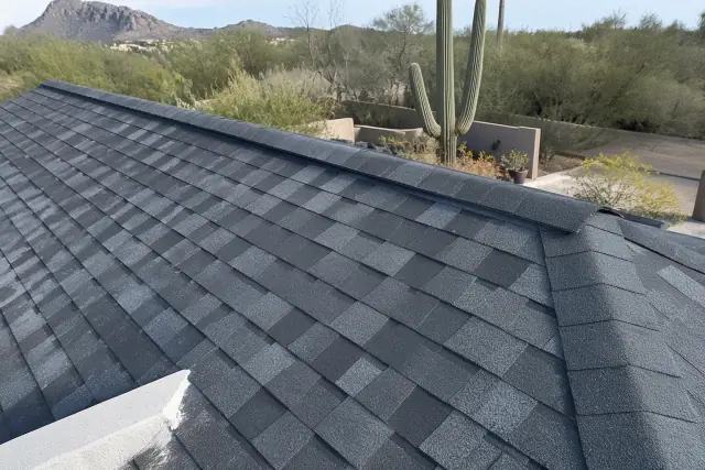 Completed asphalt shingle roof installation on a steep slope in Tucson, AZ with desert cacti in the background.