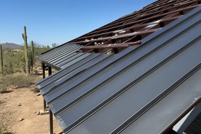 Standing seam metal roofing panels being installed on a sloped roof in Tucson, AZ with desert cacti in the background.