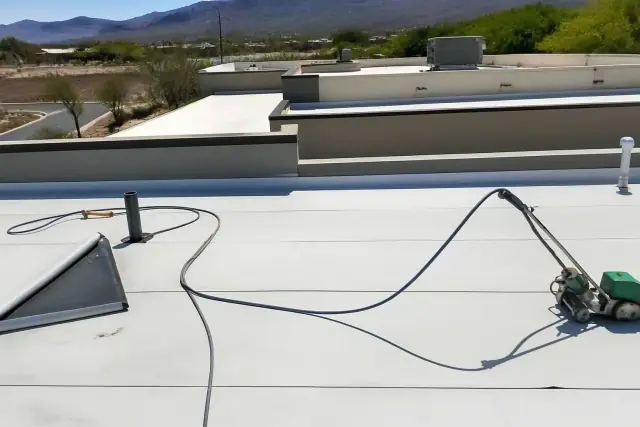 A worker applies heat-welded seams to a commercial flat roof on a sunny day in Green Valley, AZ.