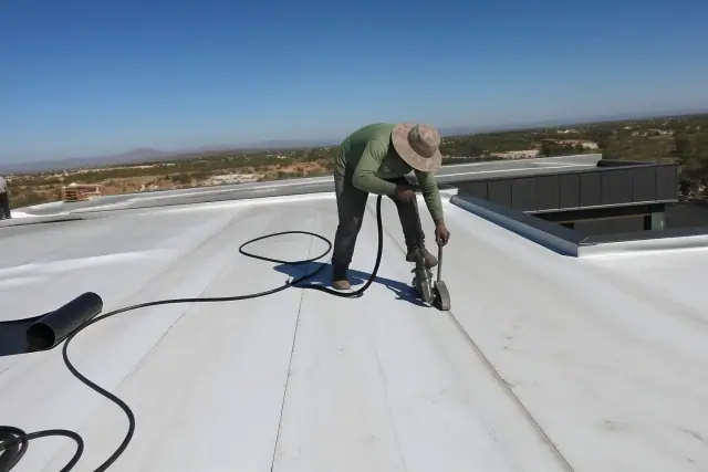 Contractor heat-welding a commercial roofing membrane on a building in Vail, AZ under a clear blue sky.