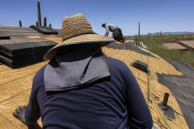 A roofing professional kneeling on a steep-sloped roof in Tucson, AZ, securing shingle bundles under desert sunlight.