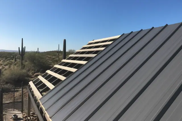 Corrugated metal panels being installed on a sloped roof frame in a Tucson, AZ desert landscape with saguaro cacti.