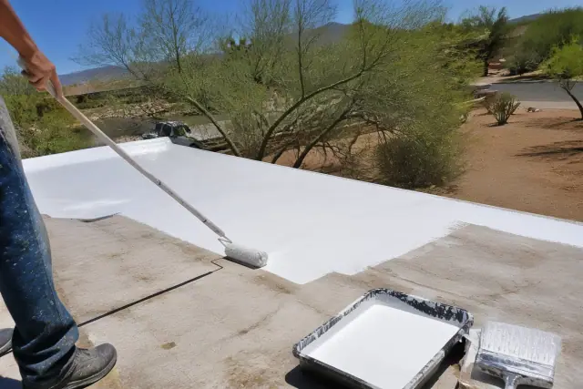 Applying white elastomeric coating to a flat roof in Tucson, AZ, with palo verde trees in the background.