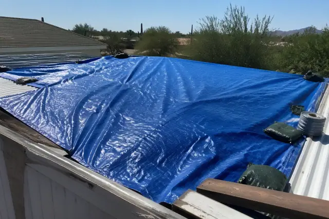 Heavy-duty tarp covering a damaged section of a residential metal roof in Tucson, AZ under harsh desert sunlight.