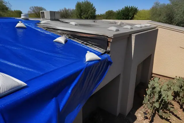 Heavy-duty tarp weighted by sandbags covering a damaged section of a residential roof in Tucson, AZ.