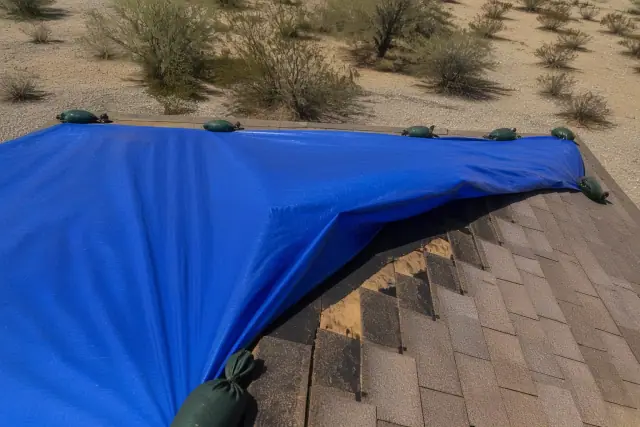 Heavy-duty tarp covering a damaged residential roof in Drexel Heights, AZ, surrounded by desert landscape.