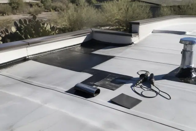 Heat-welded flat roof repair with roofing patches and tools on a commercial building rooftop in Tucson, AZ.
