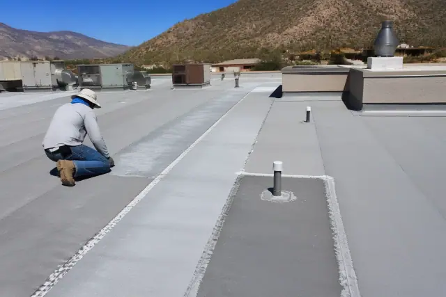 Contractor repairing a flat roof membrane with sealant near Sonoran Desert foothills in Oro Valley, AZ.