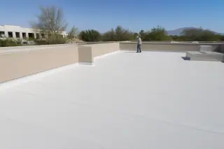 Professional inspecting a clean flat membrane roof with stucco walls and desert landscaping in Tucson, AZ.