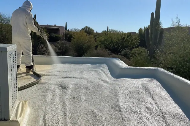 Operator spraying polyurethane foam insulation onto a residential roof in Tucson, AZ, with desert cacti in the background.