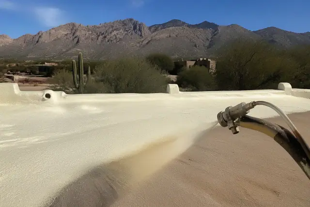 Contractor applying polyurethane foam roofing to a building in Oro Valley, AZ, with desert mountains in the background.
