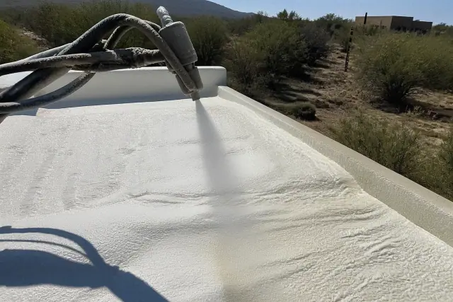 Polyurethane foam insulation being sprayed onto a roof deck in Sahuarita, AZ, with desert landscape in the background.