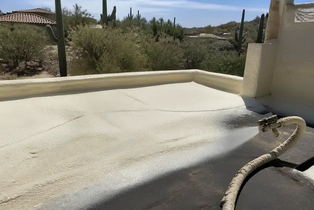 Operator applying polyurethane foam insulation to a roof at a home in Tanque Verde, AZ, surrounded by desert landscape.