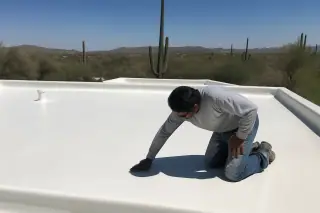 Technician inspecting a seamless white foam roof with saguaro cacti in the background in Tucson, AZ.