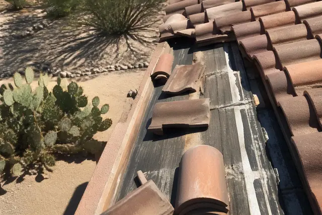 A roofer inspecting displaced clay tiles and the waterproof membrane on a roof in Tucson, AZ.