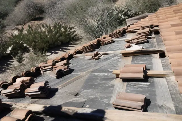 Roofer removing clay tiles to repair synthetic underlayment on a steep roof in Tucson, AZ.