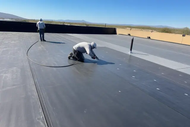 Professional applying heat-welded seams to a commercial flat roof membrane in Tucson, AZ, surrounded by desert brush.
