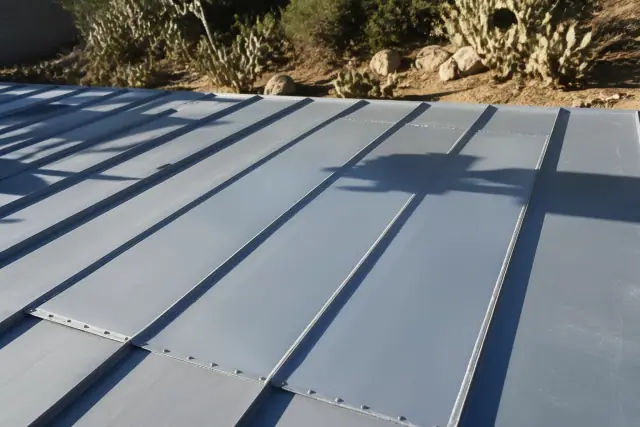 Freshly installed metal roof panels and sealant patches on a sloped residential roof in Tucson, AZ, with prickly pear cactus.