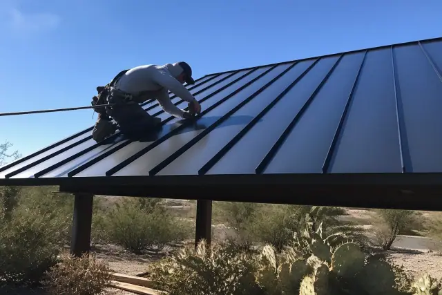 Worker installing standing seam metal roofing panels on a house framework in Casas Adobes, AZ.