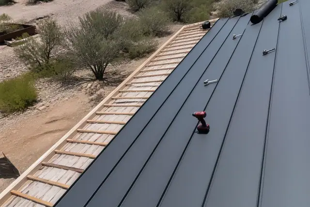 Worker installing standing seam metal panels on a residential roof in Drexel Heights, AZ.