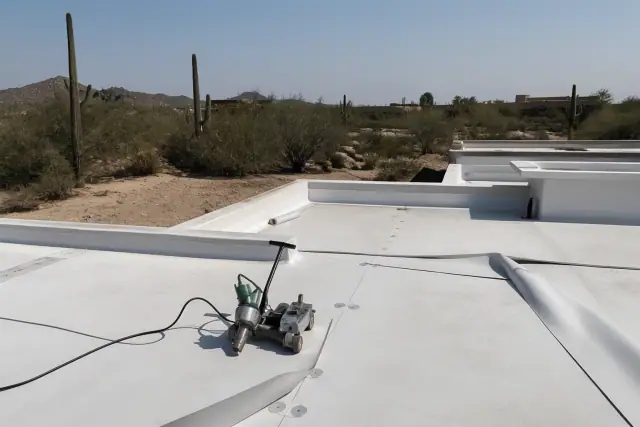 Heat-welded membrane roofing on a commercial building in Tucson, AZ with a hot-air welder and desert background.